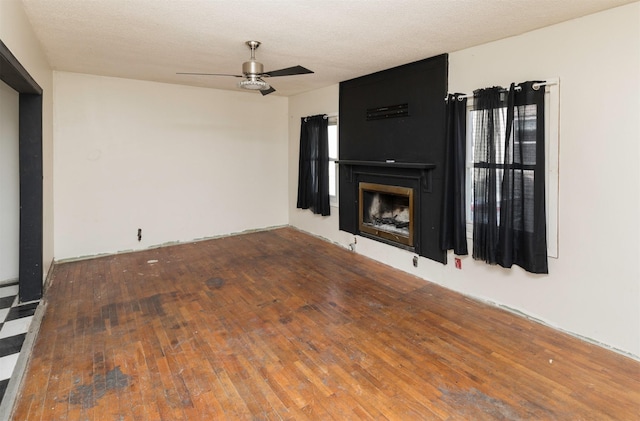 unfurnished living room featuring ceiling fan, a large fireplace, wood-type flooring, and a textured ceiling