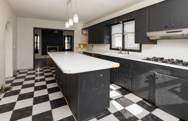 kitchen featuring white gas stovetop, a center island, sink, and hanging light fixtures