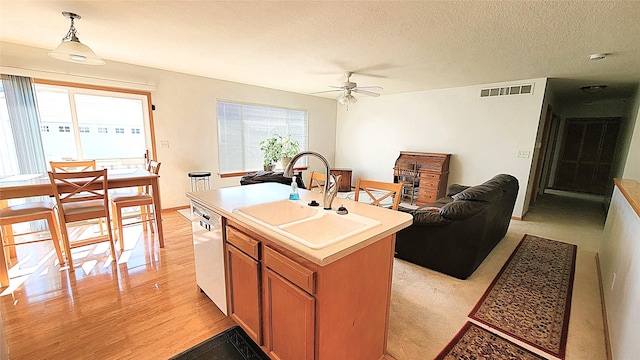 kitchen with pendant lighting, sink, dishwashing machine, a center island with sink, and light wood-type flooring