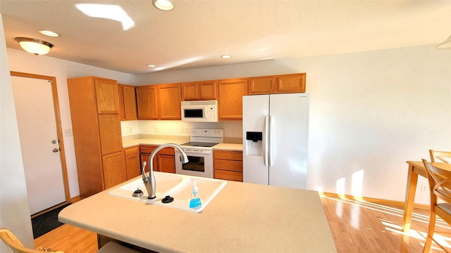 kitchen featuring sink, a textured ceiling, white appliances, and light hardwood / wood-style floors