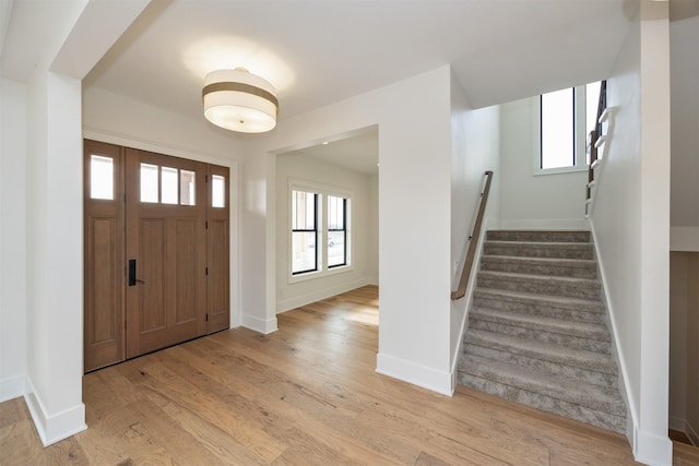 foyer entrance featuring baseboards, plenty of natural light, wood finished floors, and stairs