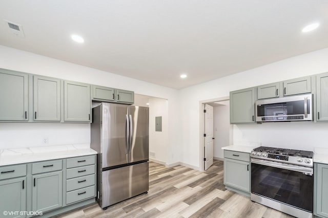 kitchen with stainless steel appliances, electric panel, light stone counters, and light hardwood / wood-style flooring