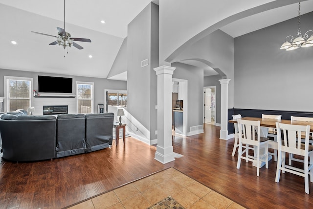 living room featuring ceiling fan with notable chandelier, high vaulted ceiling, hardwood / wood-style flooring, and ornate columns