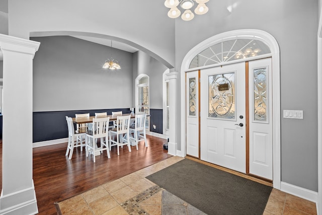 entryway featuring hardwood / wood-style flooring, a towering ceiling, a chandelier, and ornate columns