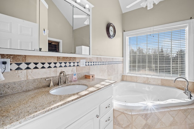 bathroom featuring ceiling fan, lofted ceiling, vanity, and tiled tub