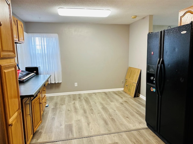 kitchen with light wood-type flooring, black fridge with ice dispenser, and a textured ceiling