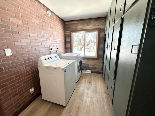 washroom featuring washing machine and dryer, brick wall, light hardwood / wood-style floors, and wood walls