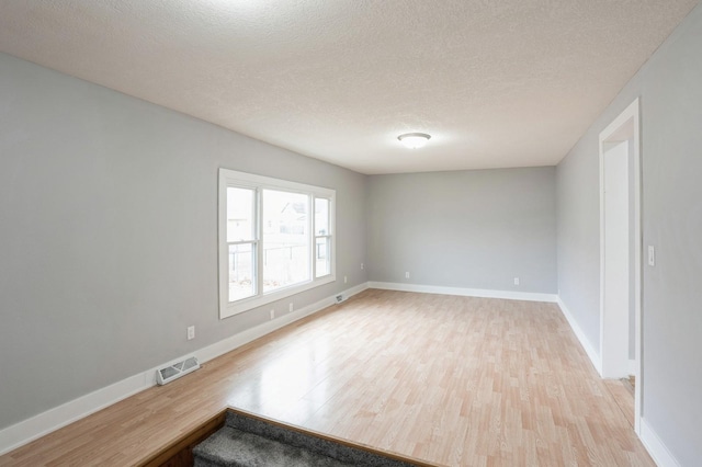 empty room with light wood-type flooring, baseboards, a textured ceiling, and visible vents