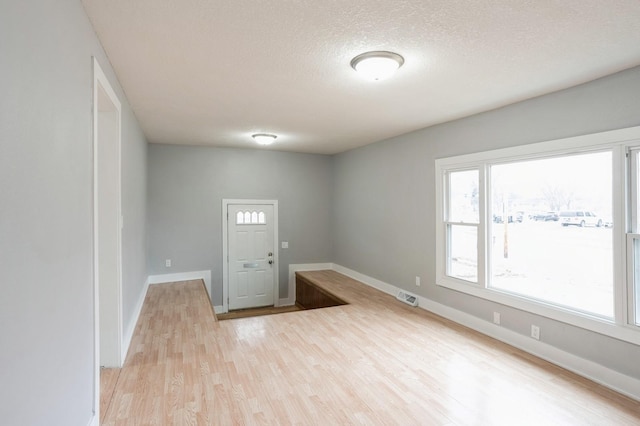 empty room with visible vents, a textured ceiling, baseboards, and wood finished floors