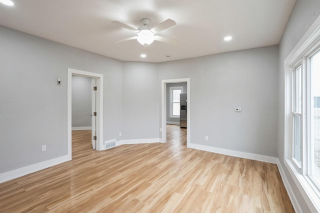 empty room featuring light wood-style flooring, a ceiling fan, visible vents, and baseboards