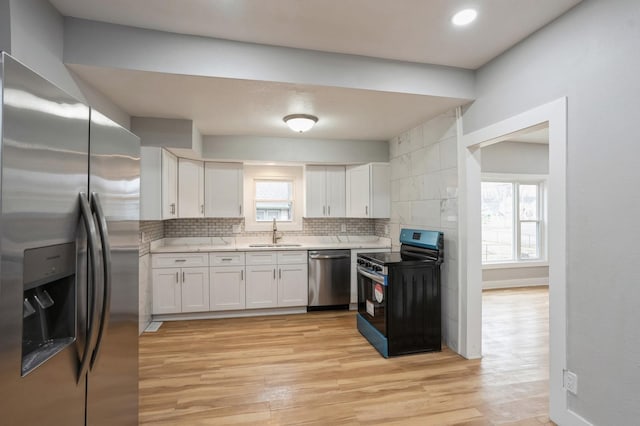 kitchen with a sink, light countertops, light wood-style floors, appliances with stainless steel finishes, and backsplash