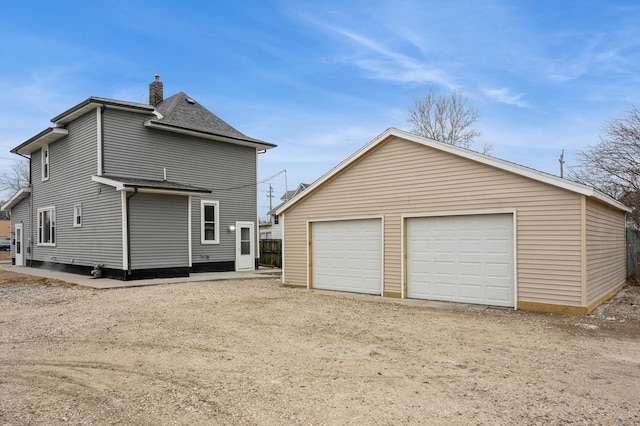 rear view of house featuring a garage, an outbuilding, roof with shingles, and a chimney