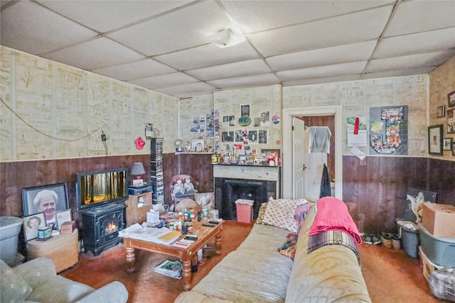 living room featuring wooden walls, a wood stove, and a drop ceiling