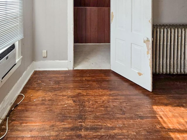 unfurnished living room with radiator heating unit, dark hardwood / wood-style floors, and wood walls