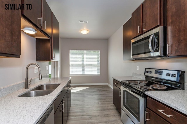 kitchen featuring appliances with stainless steel finishes, sink, light stone counters, and dark brown cabinetry