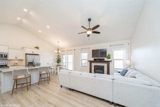 living room with high vaulted ceiling, a healthy amount of sunlight, ceiling fan with notable chandelier, and light wood-type flooring