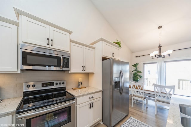 kitchen featuring stainless steel appliances, light stone countertops, vaulted ceiling, and hanging light fixtures