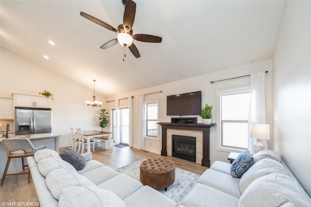 living room with vaulted ceiling, ceiling fan with notable chandelier, and light hardwood / wood-style flooring