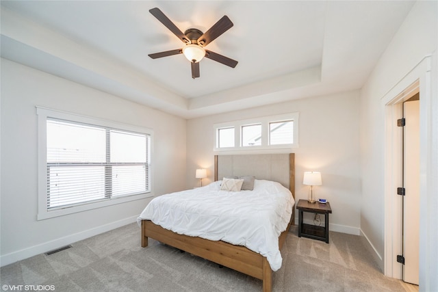 bedroom with a raised ceiling, light carpet, and ceiling fan