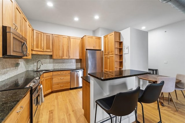 kitchen featuring sink, light hardwood / wood-style flooring, dark stone counters, a kitchen breakfast bar, and stainless steel appliances