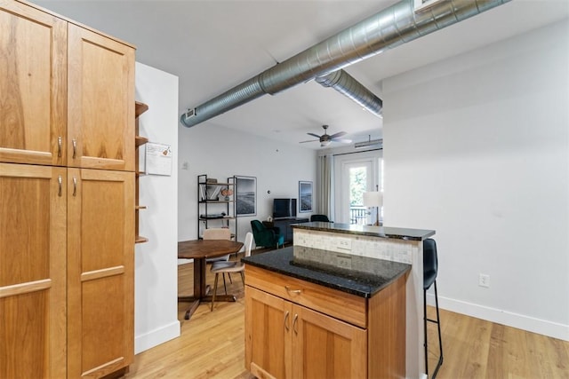 kitchen with ceiling fan, a breakfast bar, dark stone counters, and light wood-type flooring