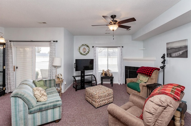 living room featuring a tiled fireplace, ceiling fan, carpet, and a textured ceiling