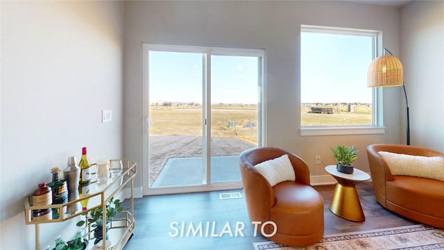 sitting room with visible vents, wood finished floors, and a healthy amount of sunlight