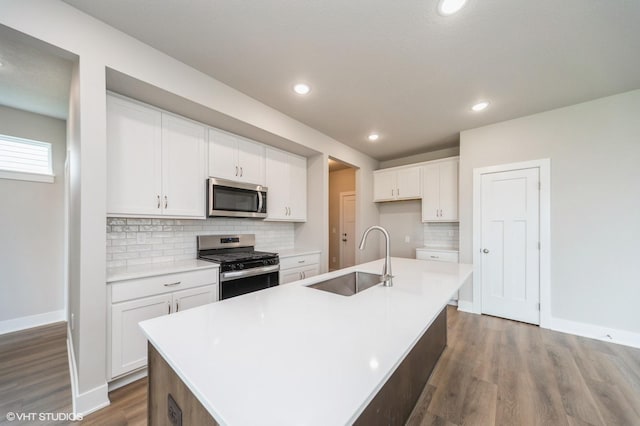 1461 S 91st St, West Des Moines, IA 50266 - kitchen with appliances with stainless steel finishes, wood finished floors, white cabinets, tasteful backsplash, and a kitchen island with sink