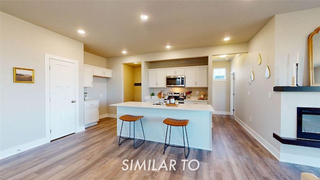kitchen featuring a kitchen island with sink, stove, stainless steel microwave, light wood finished floors, and white cabinetry