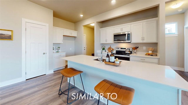 kitchen with light wood-type flooring, white cabinetry, a kitchen bar, and stainless steel appliances