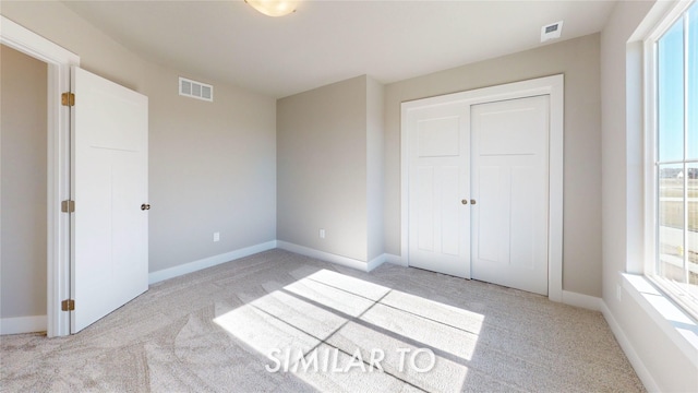 unfurnished bedroom featuring light colored carpet, baseboards, visible vents, and a closet