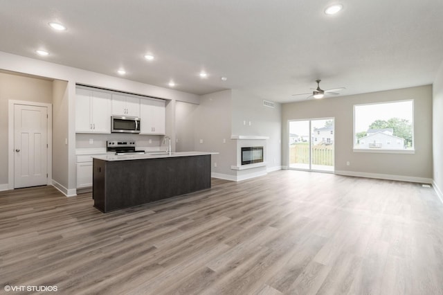 5616 Leyden Ave, Des Moines, IA 50317 - kitchen with stainless steel microwave, electric range, open floor plan, a ceiling fan, and white cabinetry