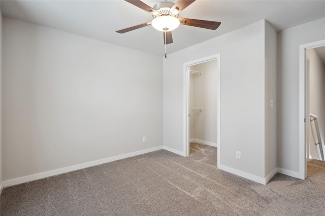 unfurnished bedroom featuring ceiling fan, a walk in closet, a closet, and light carpet