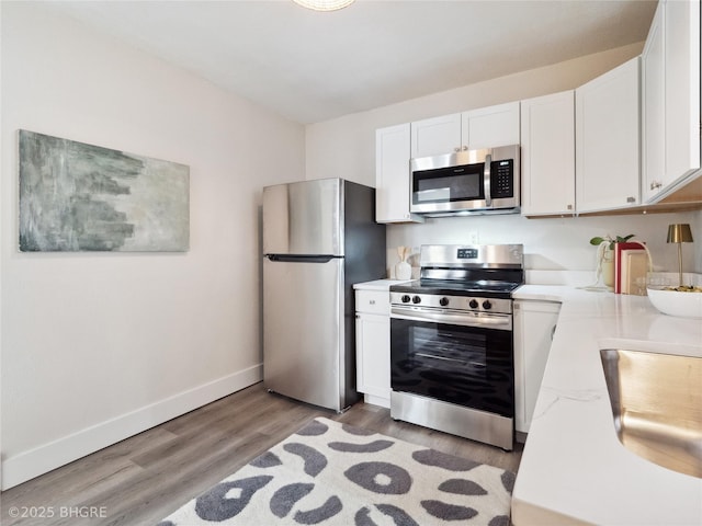 kitchen featuring appliances with stainless steel finishes, sink, light hardwood / wood-style flooring, and white cabinets