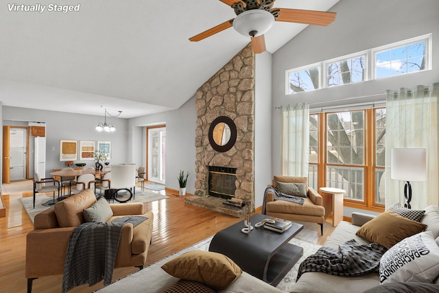 living room with high vaulted ceiling, a stone fireplace, ceiling fan with notable chandelier, and light wood-type flooring