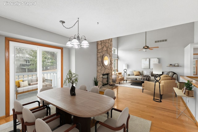 dining space featuring ceiling fan with notable chandelier, a textured ceiling, a fireplace, and light hardwood / wood-style flooring