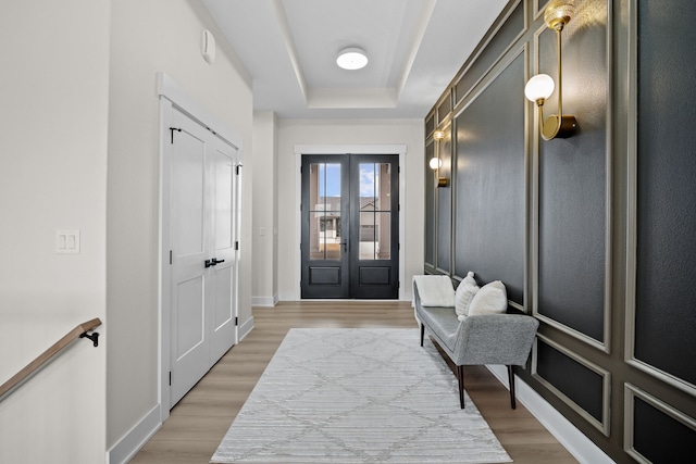 entryway featuring light wood-style flooring, a tray ceiling, baseboards, and french doors