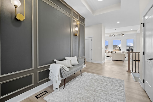 corridor with light wood-style floors, recessed lighting, a raised ceiling, and baseboards