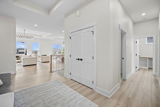 corridor with light wood-style flooring, baseboards, a raised ceiling, and recessed lighting