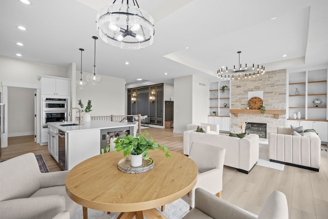 dining room featuring built in features, recessed lighting, light wood-style flooring, a stone fireplace, and a chandelier