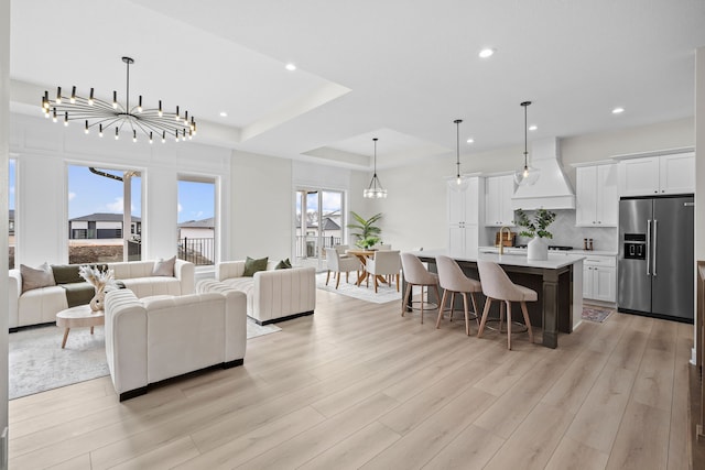 living area featuring light wood-type flooring, a raised ceiling, recessed lighting, and an inviting chandelier