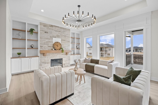 living area featuring baseboards, a tray ceiling, a stone fireplace, light wood-style floors, and built in shelves