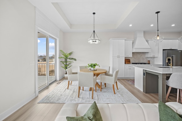 dining room featuring light wood finished floors, baseboards, a tray ceiling, and recessed lighting