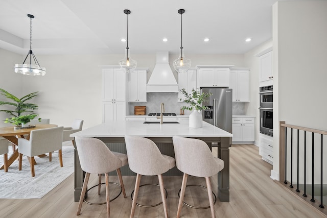 kitchen featuring appliances with stainless steel finishes, white cabinets, light wood finished floors, and custom exhaust hood