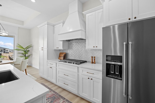 kitchen with appliances with stainless steel finishes, backsplash, light wood-style flooring, and custom range hood