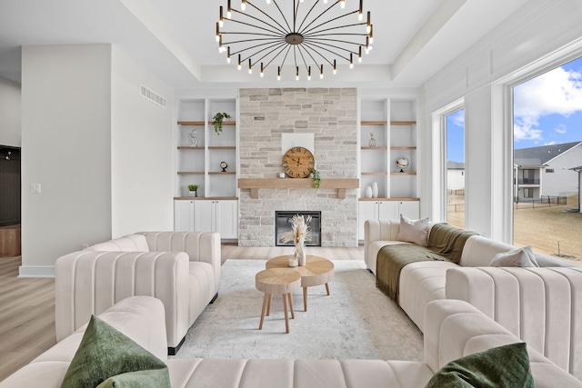 living room featuring visible vents, built in features, wood finished floors, an inviting chandelier, and a stone fireplace