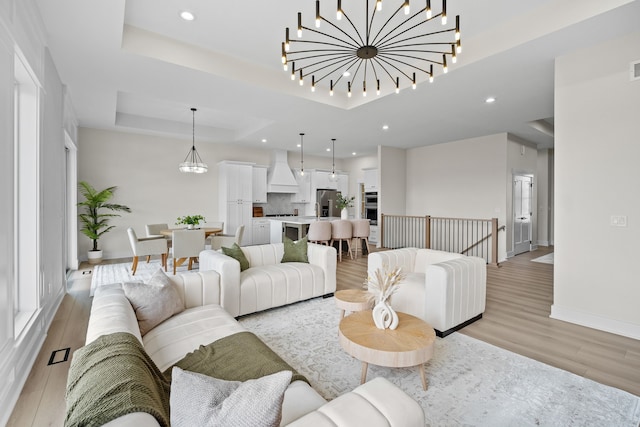 living area with light wood-style floors, a raised ceiling, a notable chandelier, and baseboards