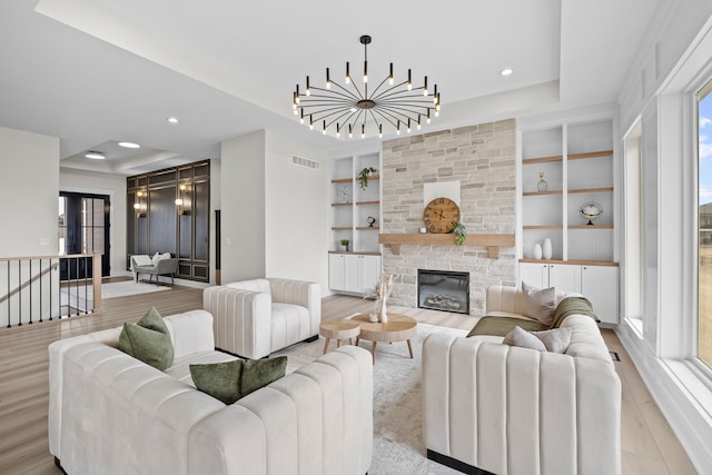 living room featuring light wood finished floors, a notable chandelier, a tray ceiling, and built in features