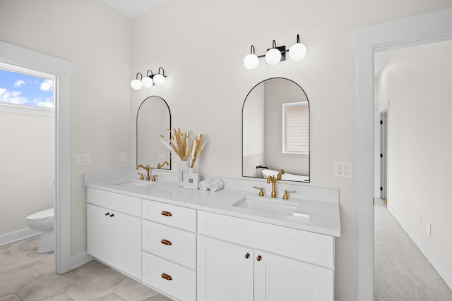 full bathroom featuring baseboards, a sink, toilet, and double vanity