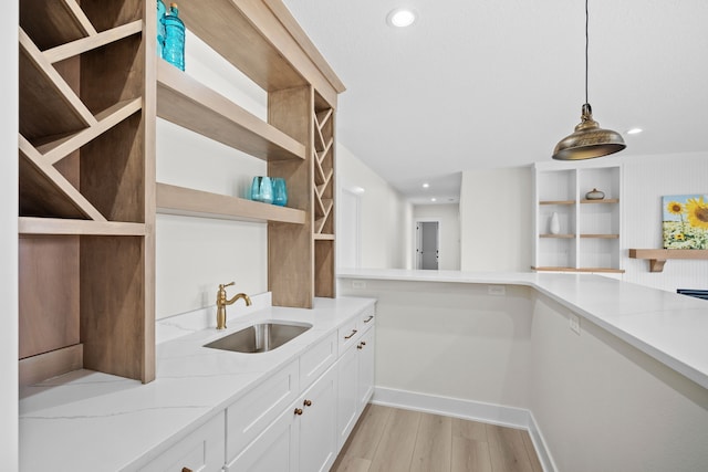 kitchen featuring light stone counters, a sink, light wood-style floors, open shelves, and decorative light fixtures